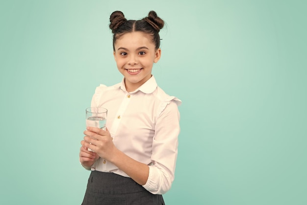 Adolescente buvant de l'eau du verre sur fond bleu isolé Santé de la vie quotidienne Heureux adolescent émotions positives et souriantes de l'adolescente