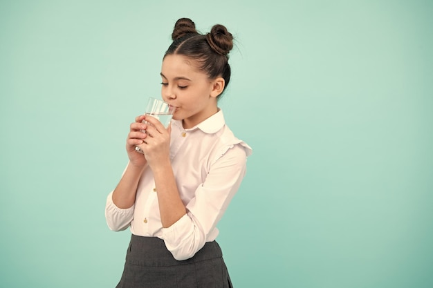 Adolescente buvant de l'eau du verre sur fond bleu Santé de la vie quotidienne Boire de l'eau pour les soins de santé et l'équilibre corporel Déshydratation de l'enfant assoiffé