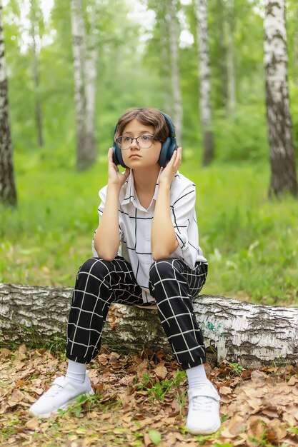 Une adolescente avec un casque écoute de la musique dans un parc de la ville, des loisirs de plein air pour les jeunes