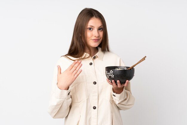 Adolescente caucasienne fille isolée sur blanc invitant à venir avec la main. Heureux que tu sois venu en tenant un bol de nouilles avec des baguettes