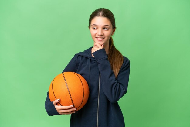 Adolescente caucasienne jouant au basket-ball sur fond isolé regardant sur le côté et souriant