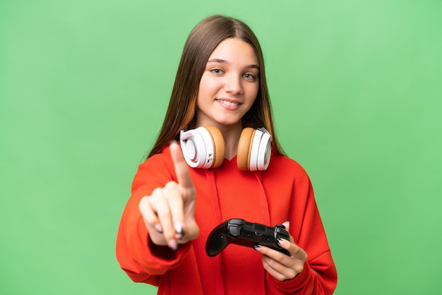 Adolescente caucasienne jouant avec un contrôleur de jeu vidéo sur fond isolé montrant et levant un doigt