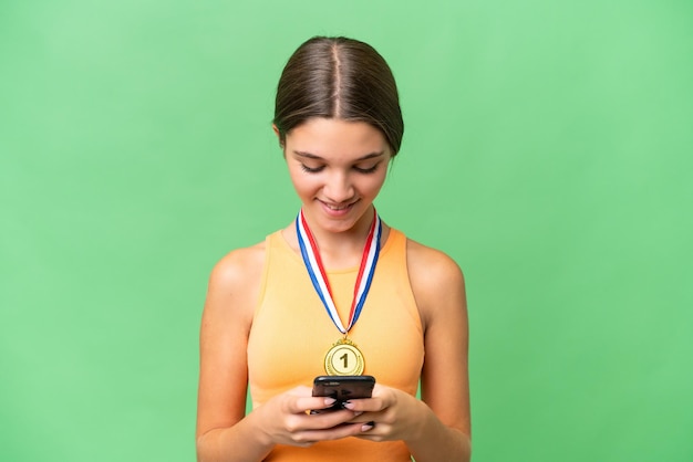 Adolescente caucasienne avec des médailles sur fond isolé envoyant un message avec le mobile