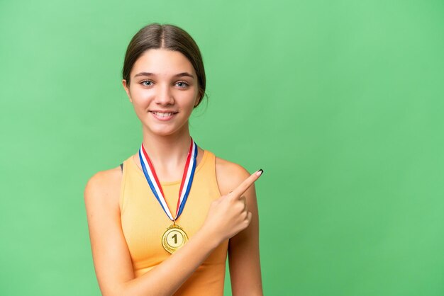 Adolescente caucasienne avec des médailles sur fond isolé pointant vers le côté pour présenter un produit