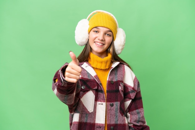 Adolescente caucasienne portant des manchons d'hiver sur fond isolé avec les pouces vers le haut parce que quelque chose de bien s'est produit