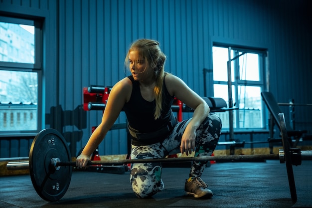 Adolescente caucasienne pratiquant l'haltérophilie dans la salle de gym. Modèle sportif féminin se préparant à l'entraînement avec haltères, semble concentré. Musculation, mode de vie sain, concept de mouvement et d'action.