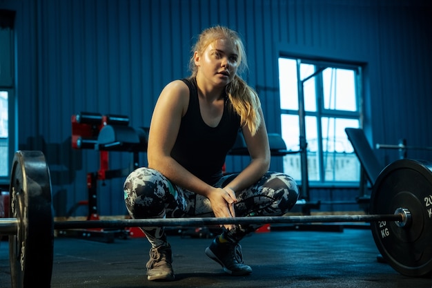 Adolescente caucasienne pratiquant l'haltérophilie dans la salle de gym. Modèle sportif féminin se préparant à l'entraînement avec haltères, semble concentré. Musculation, mode de vie sain, concept de mouvement et d'action.