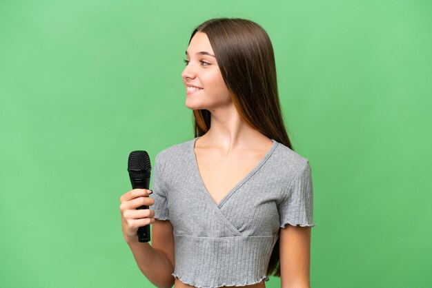 Adolescente chanteuse prenant un microphone sur fond isolé regardant du côté