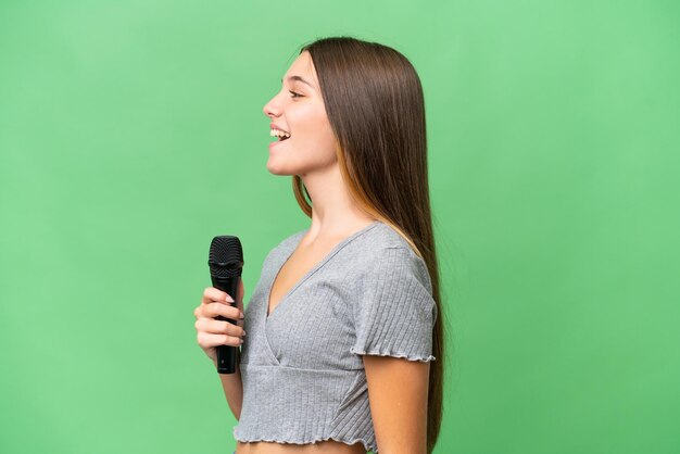 Adolescente chanteuse prenant un microphone sur fond isolé riant en position latérale