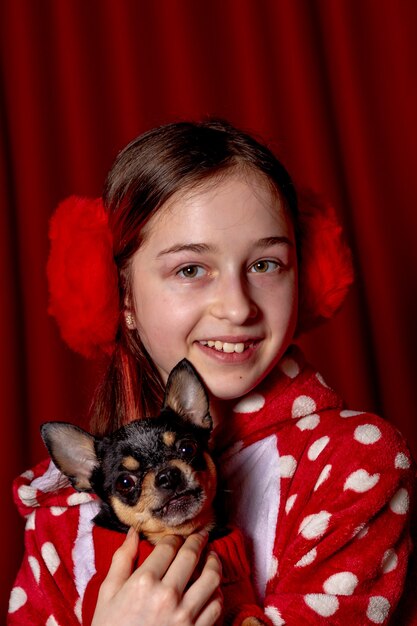 Adolescente et un chihuahua vêtu d'un pull rouge pour chiens à la maison sur fond rouge.