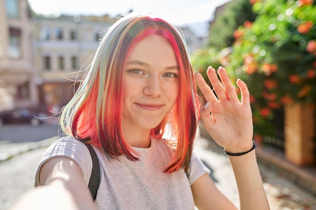 Adolescente avec une coiffure à la mode, une jeune blogueuse d'art de la mode enregistre un flux en ville, des regards féminins dans la webcam d'un smartphone, des gestes et des discussions, un visage en gros plan