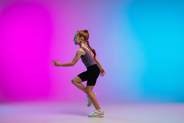 Adolescente courir, faire du jogging sur fond de studio néon rose-bleu dégradé en mouvement