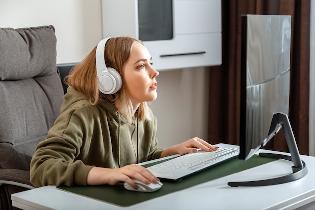 Une adolescente cybersportive gamer joue à un jeu informatique en ligne seul à la maison pendant son temps libre. Jeune femme blonde au casque jouer avec enthousiasme au flux de jeux vidéo sur ordinateur pc.