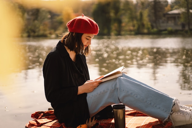 Une adolescente dans un livre de lecture de béret rouge sur la saison d'automne de ponton en bois