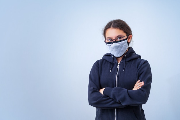 Adolescente dans un masque médical se tient les bras croisés, sur un fond gris froid avec copie espace. Virus.