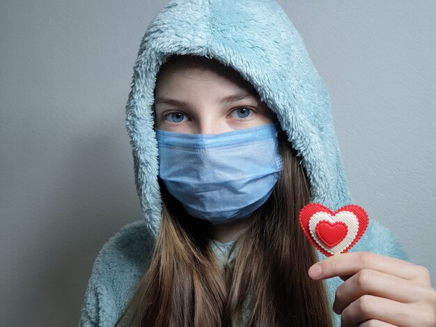 Adolescente dans un masque médical tient un coeur rouge dans sa main, la Saint-Valentin en quarantaine