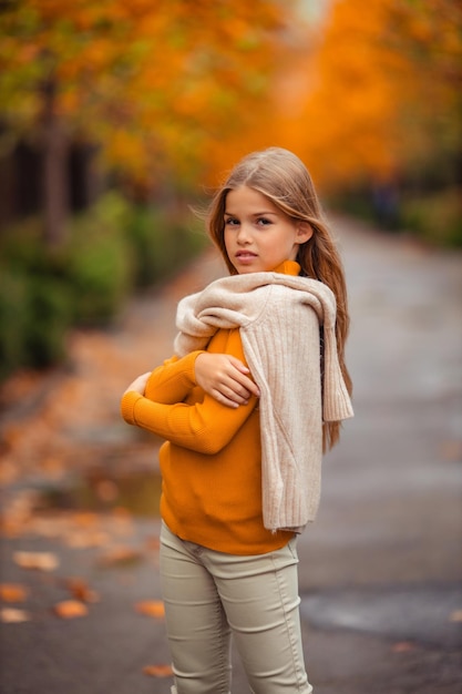 une adolescente dans un pull jaune se promène le long d'une rue en dehors de la ville sur la toile de fond des arbres jaunes promenade amusante en automne