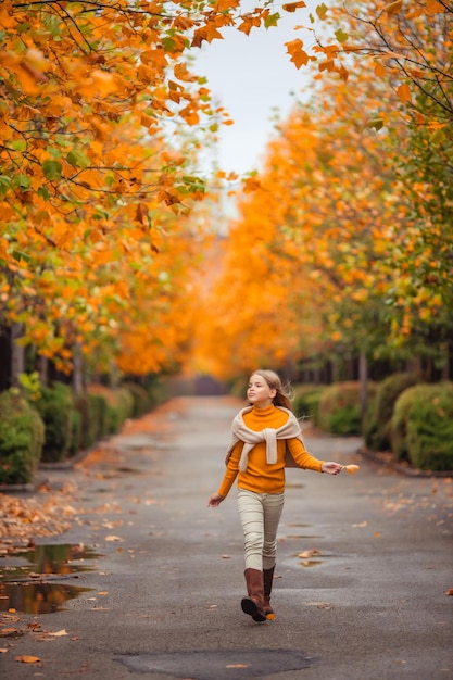 Photo une adolescente dans un pull jaune se promène le long d'une rue en dehors de la ville sur la toile de fond des arbres jaunes promenade amusante en automne