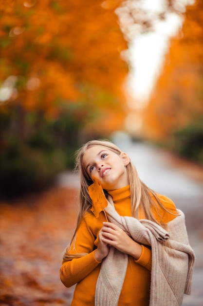 une adolescente dans un pull jaune se promène le long d'une rue en dehors de la ville sur la toile de fond des arbres jaunes promenade amusante en automne