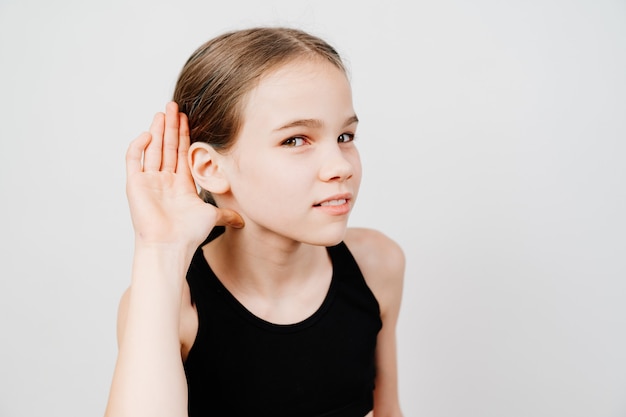 Une adolescente dans un T-shirt noir tient sa main par son oreille et écoute.