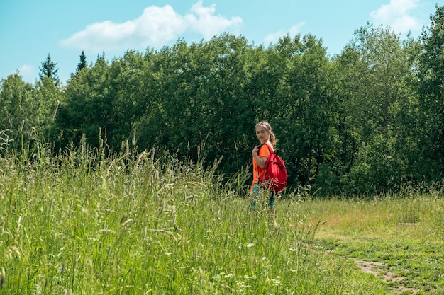 Une adolescente dans un t-shirt orange vif avec un sac à dos se promène dans la nature