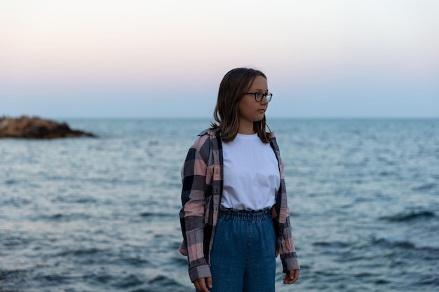 Adolescente debout au bord de la mer au coucher du soleil