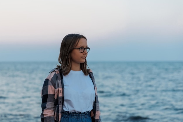 Adolescente debout au bord de la mer au coucher du soleil