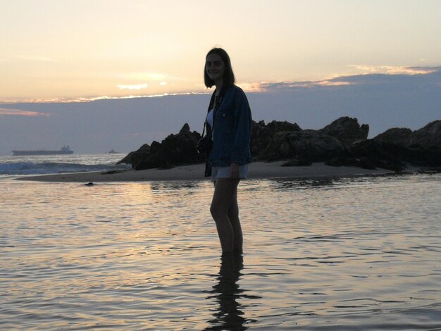 Photo une adolescente debout dans la mer contre le ciel au coucher du soleil