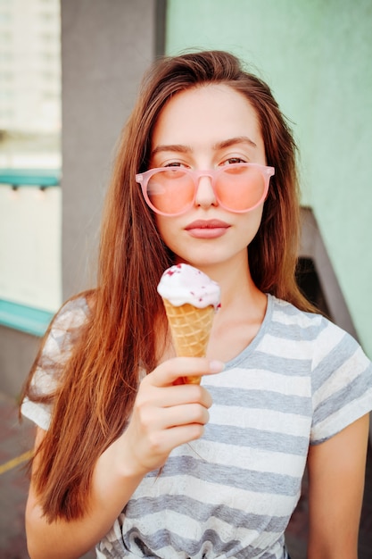 Adolescente drôle dans des lunettes de soleil cool hipster mangeant un cornet de crème glacée. Nourriture d'été