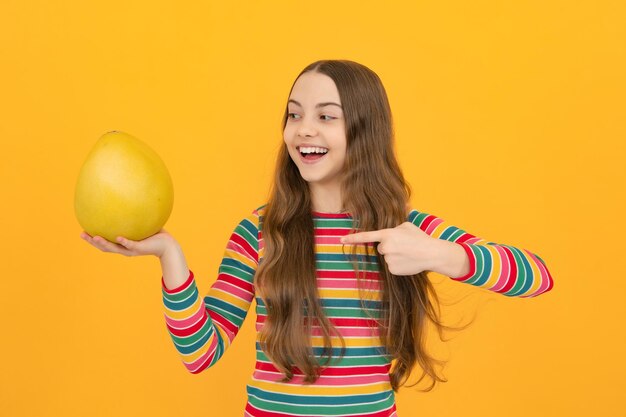 Une adolescente drôle tient un pomelo d'agrumes ou un pomelo gros pamplemousse vert isolé sur fond jaune