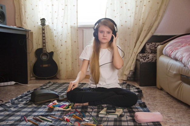 Adolescente écoutant de la musique dans des écouteurs assis par terre à la maison, passe-temps des jeunes