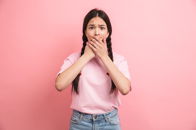 adolescente effrayée avec deux tresses regardant devant et couvrant sa bouche isolée sur un mur rose