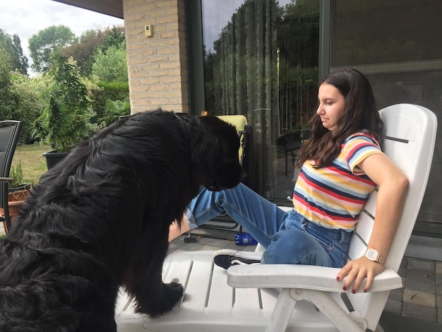 Une adolescente effrayée regarde un chien noir sur une chaise devant la maison.