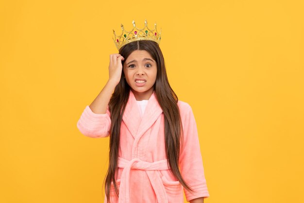 Adolescente égoïste confuse dans un peignoir en éponge à la maison et une couronne de princesse confuse