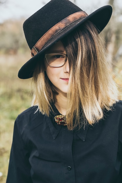 Une adolescente élégante avec un chapeau noir, des lunettes, un sourire se penche sur l&#39;appareil photo.