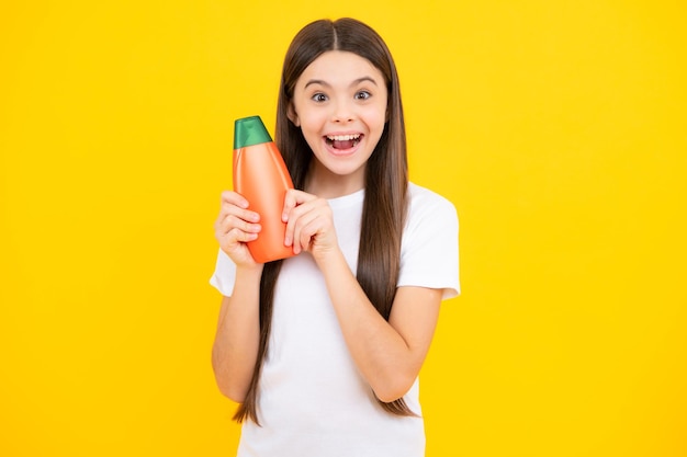 Adolescente enfant fille montrant des conditionneurs de shampoing en bouteille ou un gel douche isolé sur fond jaune Produit cosmétique pour cheveux Maquette bouteille Adolescent excité heureux d'émotions étonnées et ravies