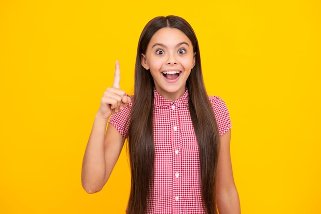 Adolescente étonnée Expression excitée joyeuse et heureuse Portrait de jeune adolescente pointant vers le haut avec le doigt isolé sur fond jaune