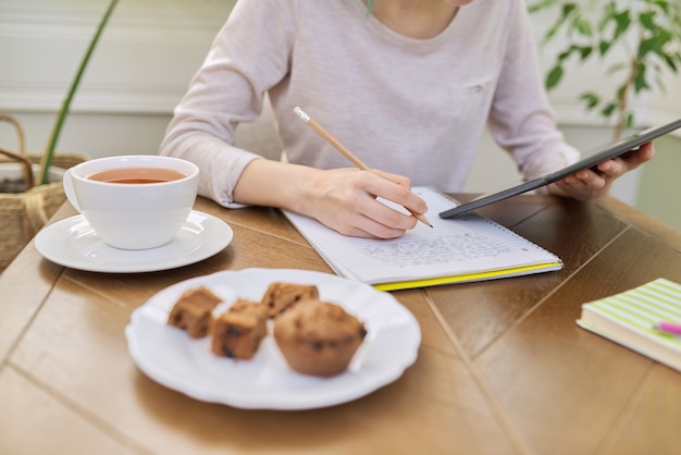 Adolescente étudiant à la maison, jeune étudiant assis à table à l'aide d'une tablette numérique, cahiers d'école, manuels. Apprentissage à distance en ligne, technologie, concept d'éducation