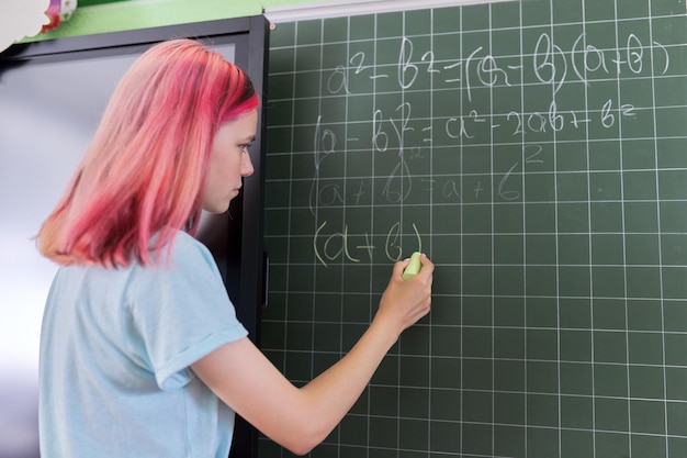 Adolescente étudiante à une leçon de mathématiques écrit à la craie sur un tableau noir. Éducation, adolescence, lycée