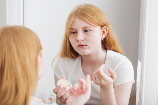 Adolescente examine l'acné devant le miroir