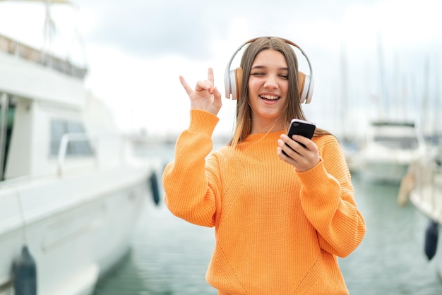 Adolescente à l'extérieur écoutant de la musique avec un mobile faisant un geste rock