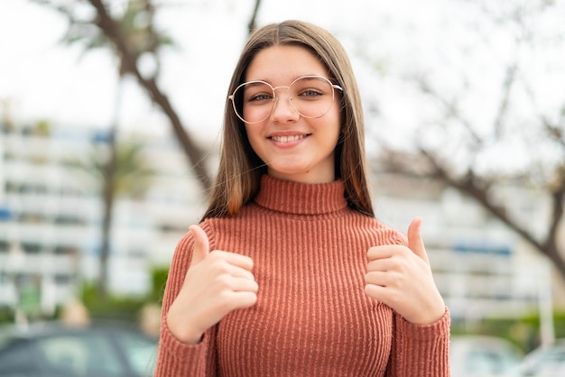 Photo adolescente à l'extérieur avec le geste du pouce levé et souriant