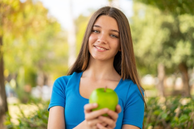 Adolescente à l'extérieur tenant une pomme avec une expression heureuse