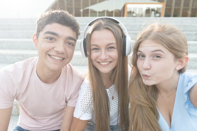 Adolescente faisant un geste de baiser et prenant un selfie avec ses amis souriants assis dans les escaliers