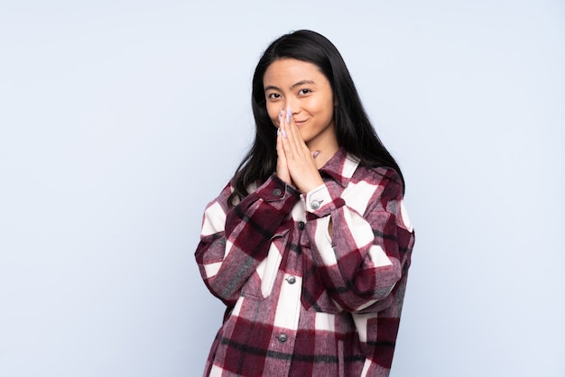 Adolescente femme chinoise isolée sur fond bleu garde la paume ensemble. La personne demande quelque chose