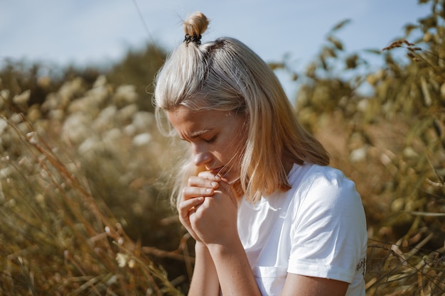 Une adolescente ferma les yeux en priant dans un champ. Mains jointes dans la foi de prière, la spiritualité et le concept de religion.