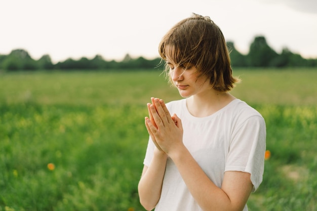 Une adolescente a fermé les yeux en priant, les mains jointes dans le concept de prière pour la foi, la spiritualité et la religion, la paix, l'espoir, les rêves, concept