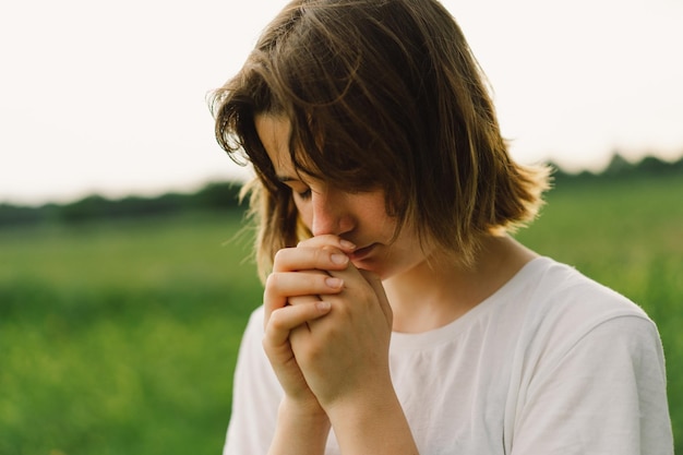 Une adolescente a fermé les yeux en priant, les mains jointes dans le concept de prière pour la foi, la spiritualité et la religion, la paix, l'espoir, les rêves, concept