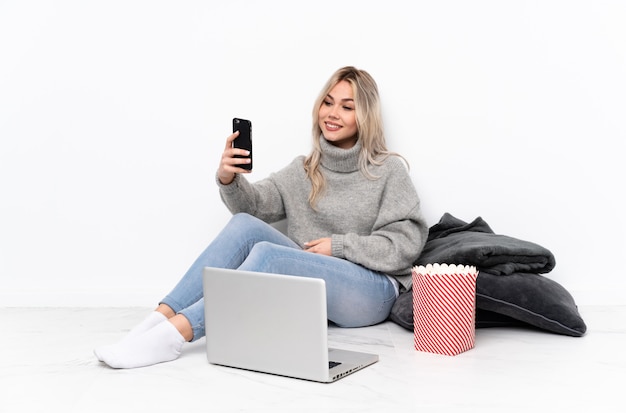Adolescente fille blonde mangeant du pop-corn tout en regardant un film sur l'ordinateur portable faisant un selfie