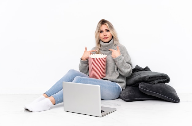 Adolescente fille blonde mangeant du pop-corn tout en regardant un film sur l'ordinateur portable